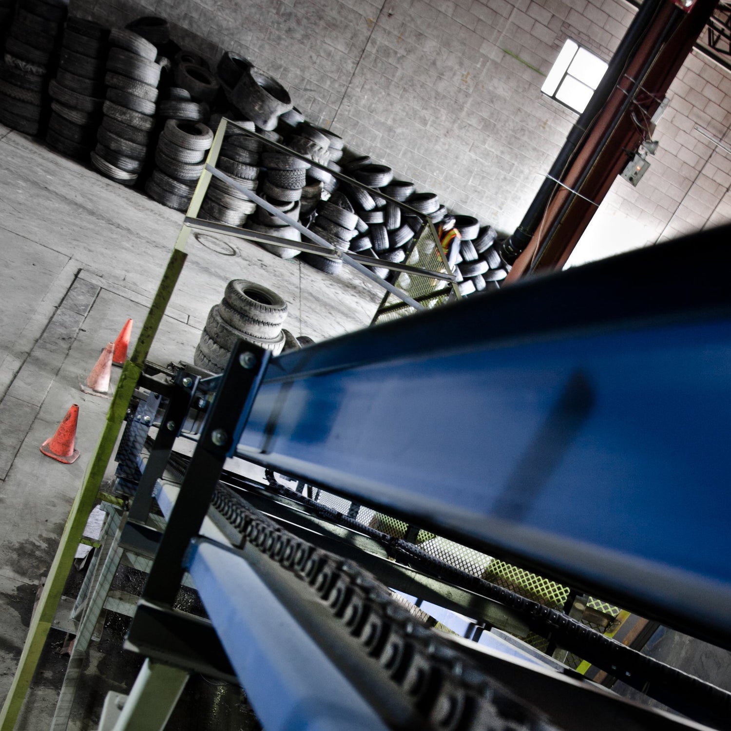 Close-up of a blue and black mechanical component in an industrial setting with tires in the background.